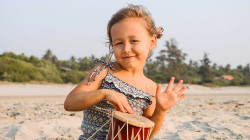 Portrait of smiling girl playing drum while sitting at beach