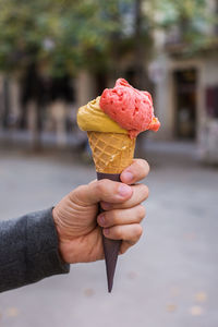 Man holding an ice cream in the street. outdoors, urban, city landscape, takeaway food