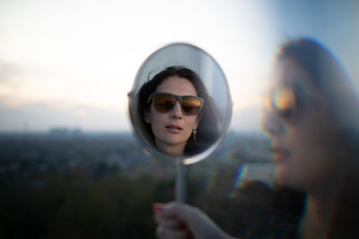 Portrait of woman wearing sunglasses while reflecting on mirror