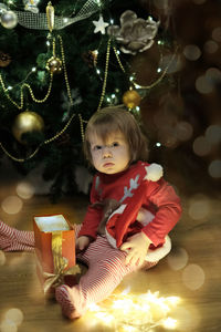 Full length of cute girl sitting on illuminated christmas tree