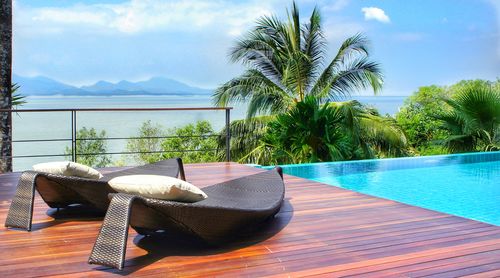 Chairs and tables by swimming pool against sky