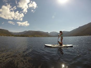 Side view of woman paddleboarding and dog in grand lake against sky