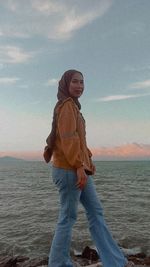 Full length of smiling woman standing in sea against sky