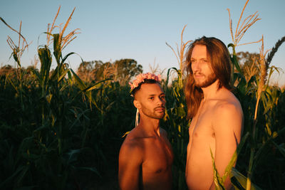 Shirtless gay men looking away while standing amidst plants