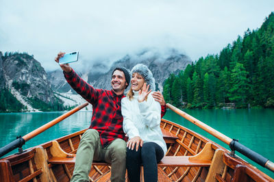 Full length of man photographing while sitting on lake against mountains