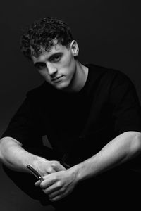 Portrait of young man sitting against black background