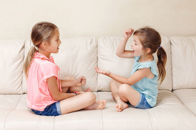 Side view of sisters playing while sitting on sofa at home