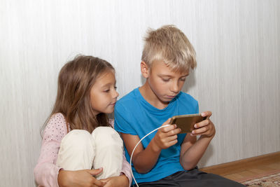 Cute boy using smart phone while sitting floor with sister at home