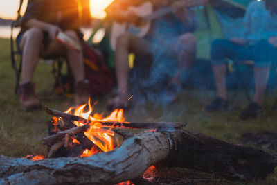 Close-up of campfire near friends sitting on chairs 