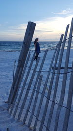 Man sitting on beach against sky during sunset