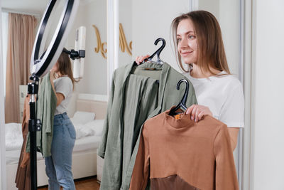 Female blogger recording vlog video on smartphone at home online influencer on near wardrobe