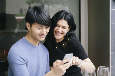 Happy friends looking at camera while using mobile phone