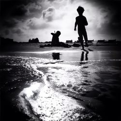 Children playing on beach against cloudy sky on sunny day