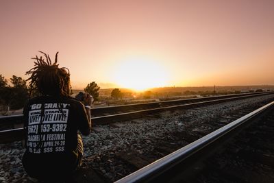 Rear view of man on railroad track against sky during sunset