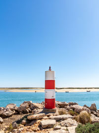 Lighthouse by sea against clear blue sky