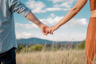 Midsection of couple holding hands while standing on field