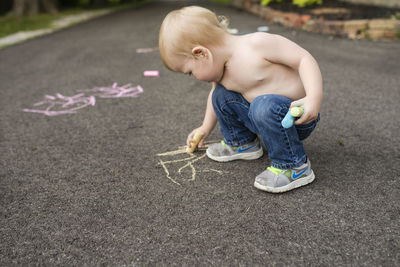 Shirtless boy writing with chalk on footpath