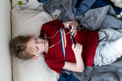 Top down view of teen watching phone with earbuds in ears lying on bed