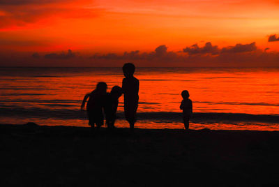 Silhouette people on beach against orange sky