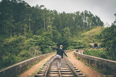 Woman walking on railroad track against trees