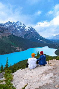 Rear view of people sitting on mountain against sky