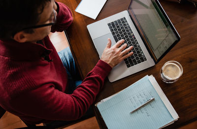 Overhead image of man working from home using computer at wooden table