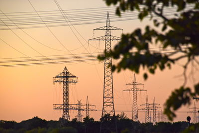 Low angle view of electricity pylon against sky during sunset