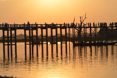 Wooden posts in sea against orange sky