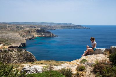 Woman sitting on cliff against sea