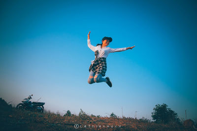 Full length of man jumping against blue sky