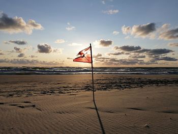 Scenic view of beach and red flag against sky during sunset