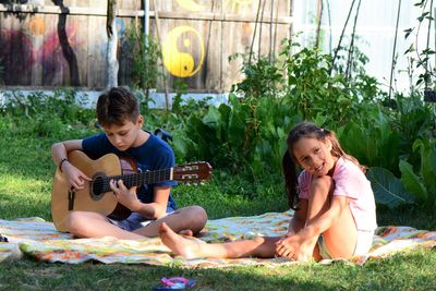 Boy playing guitar while sitting with girl at park