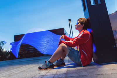 Side view of woman sitting against blue sky