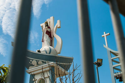 Low angle view of jesus christ against sky seen through fence