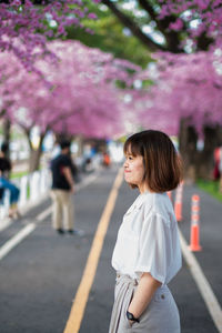 Woman standing by cherry blossom on road in city