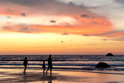 Silhouette people on beach against sky during sunset