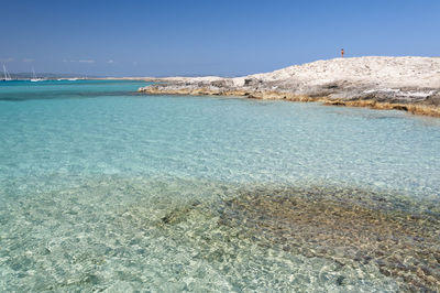 The beach of ses illetas, formentera. a person on the top of the rock observes the mediterranean sea