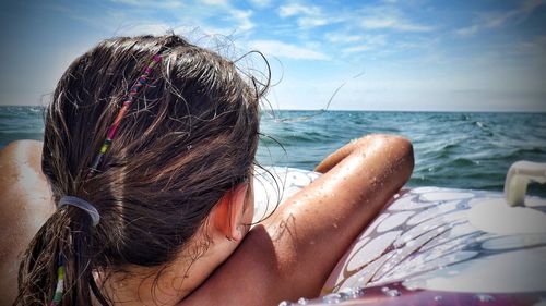 Rear view of woman relaxing on beach against sky