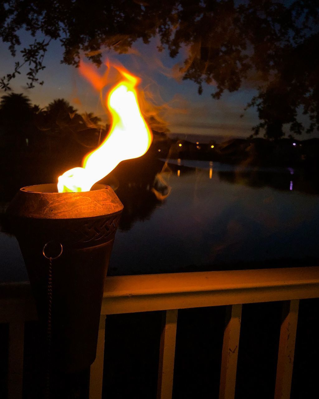 CLOSE-UP OF BURNING CANDLE AGAINST RAILING AT SUNSET