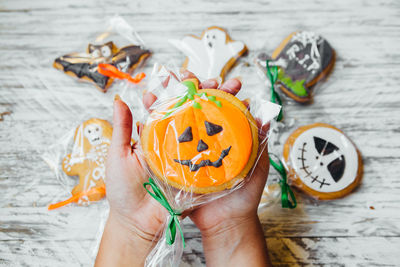 Cropped hands of woman holding various cookies wrapped in plastic over wooden table during halloween
