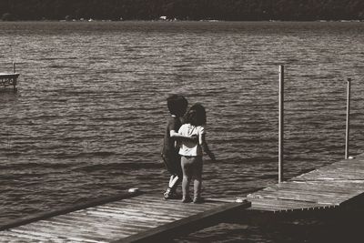 Rear view of couple standing on jetty against sea