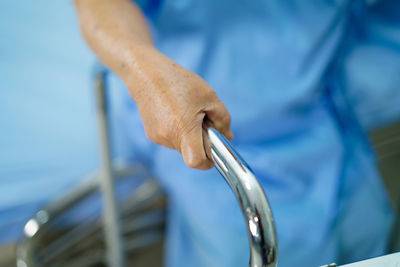 Midsection of woman holding mobility walker while sitting on hospital bed
