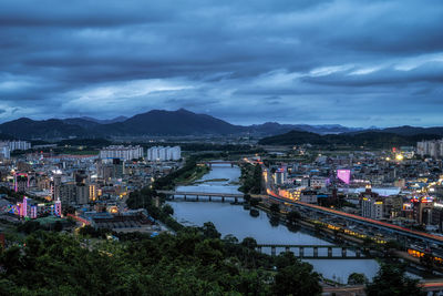 High angle view of illuminated city by river against sky