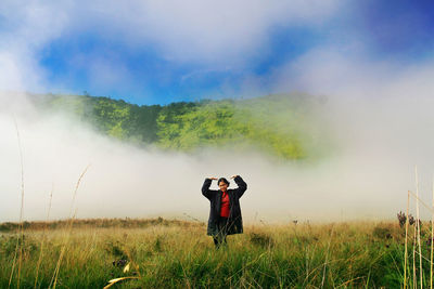 Young woman standing on field against mountain during foggy weather