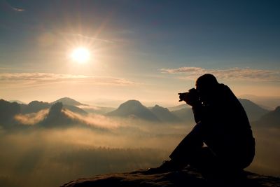 Happy photo enthusiast is enjoying fantastic miracle of nature on cliff on rock.