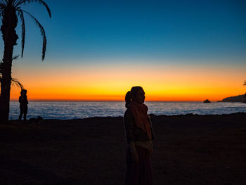 Woman standing at beach against sky during sunset