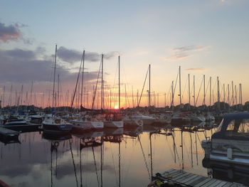 Sailboats moored in harbor at sunset