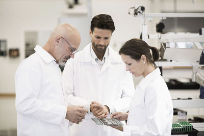 Team of technicians examining circuit board in factory