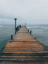 Wooden jetty leading to pier over sea against sky