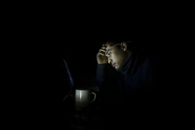 Tensed man using laptop in darkroom